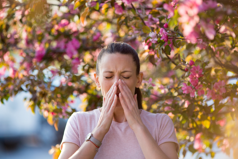 woman sneezing under flowering tree