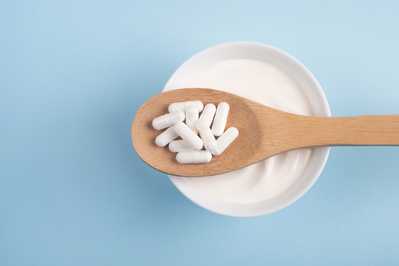 probiotic supplements on a wooden spoon over a bowl of yogurt