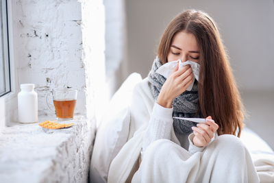 young woman with flu looking at thermometer while holding a tissue over her nose