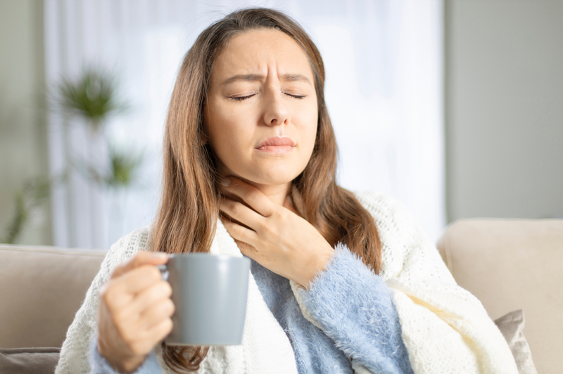 woman with a sore throat holding her neck and a mug of tea